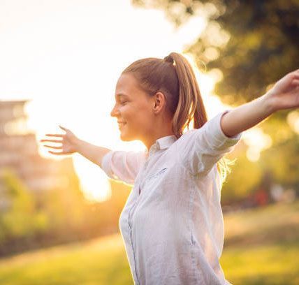 A woman is standing in a park with her arms outstretched.