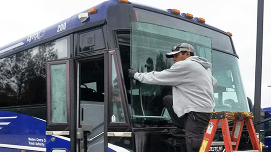 A man is working on the windshield of a bus.