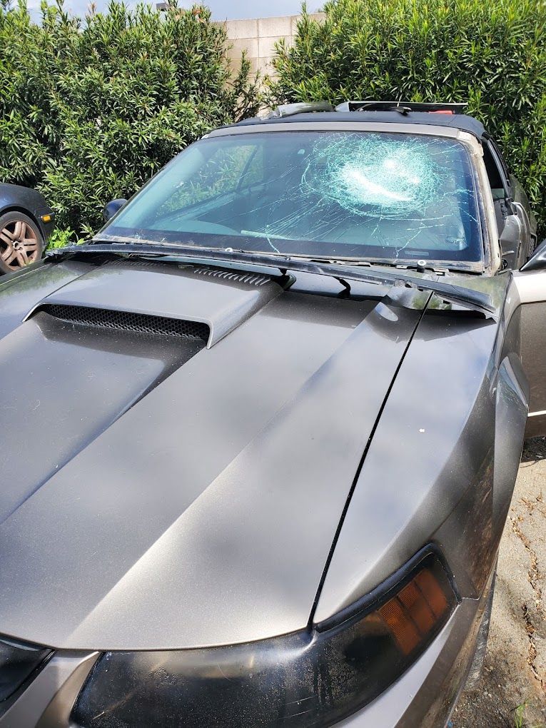 A car with a broken windshield is parked in a driveway.