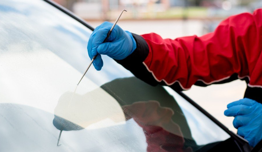 A man in a red jacket and blue gloves is cleaning the windshield of a car.