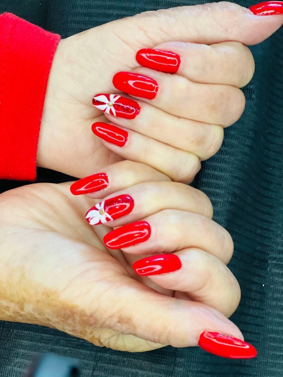 Hands with red nail polish, two nails with white floral accents.