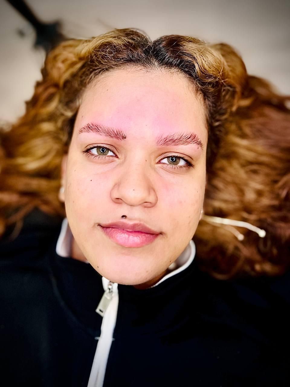 Woman with newly microbladed eyebrows; light skin, green eyes, black zip-up jacket.