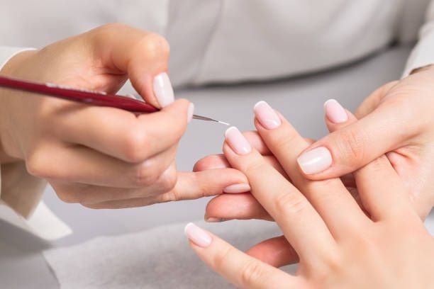Hand with oval-shaped nails painted in a soft pink hue, extended against a matching pink background.