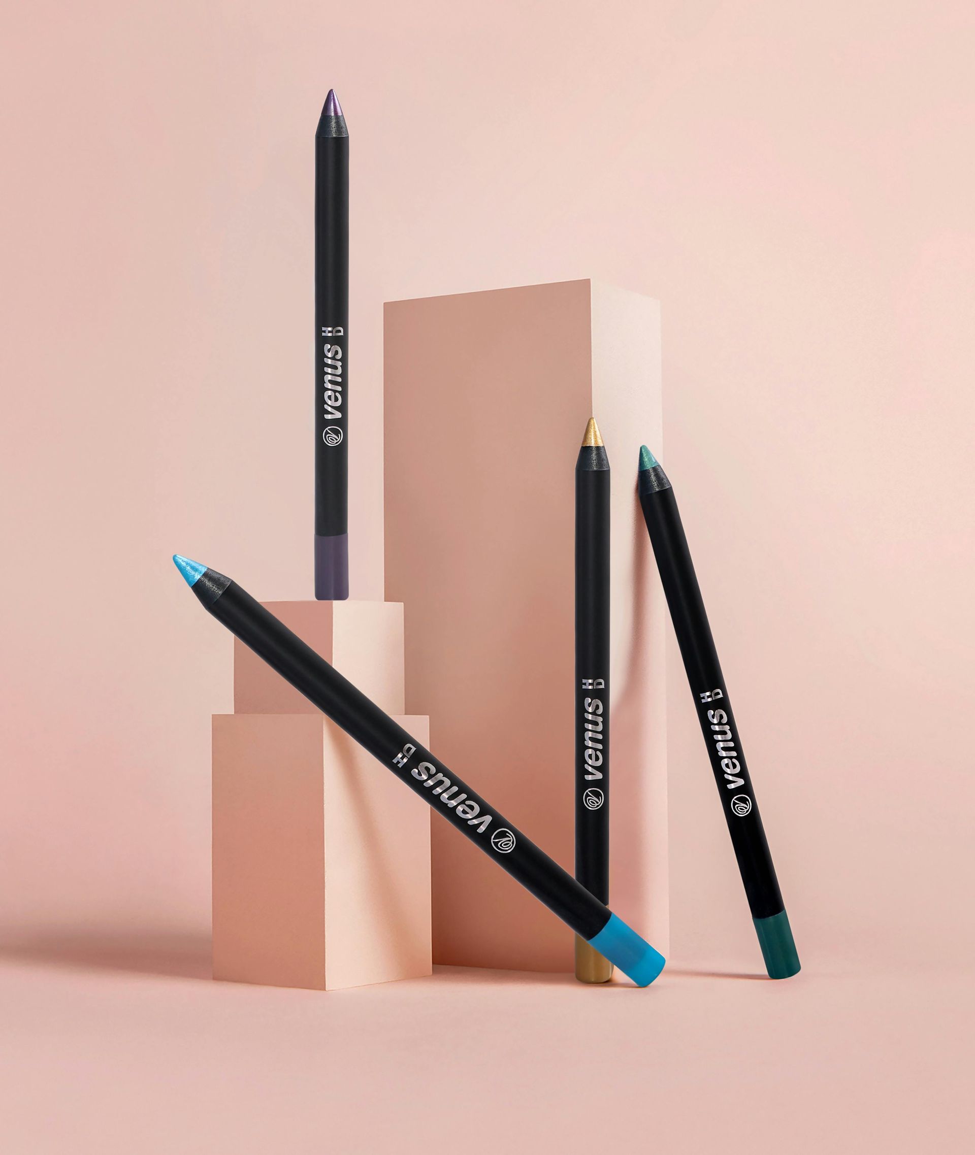 Four eyeliner pencils are stacked on top of each other on a pink surface.