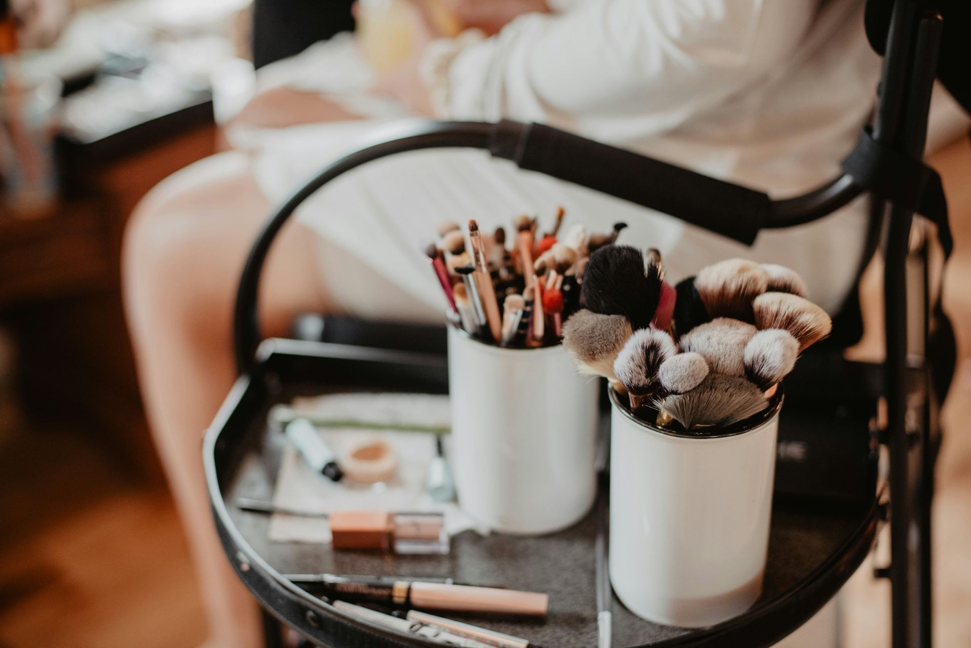 Makeup brushes in white containers on a tray; person in background, getting ready.