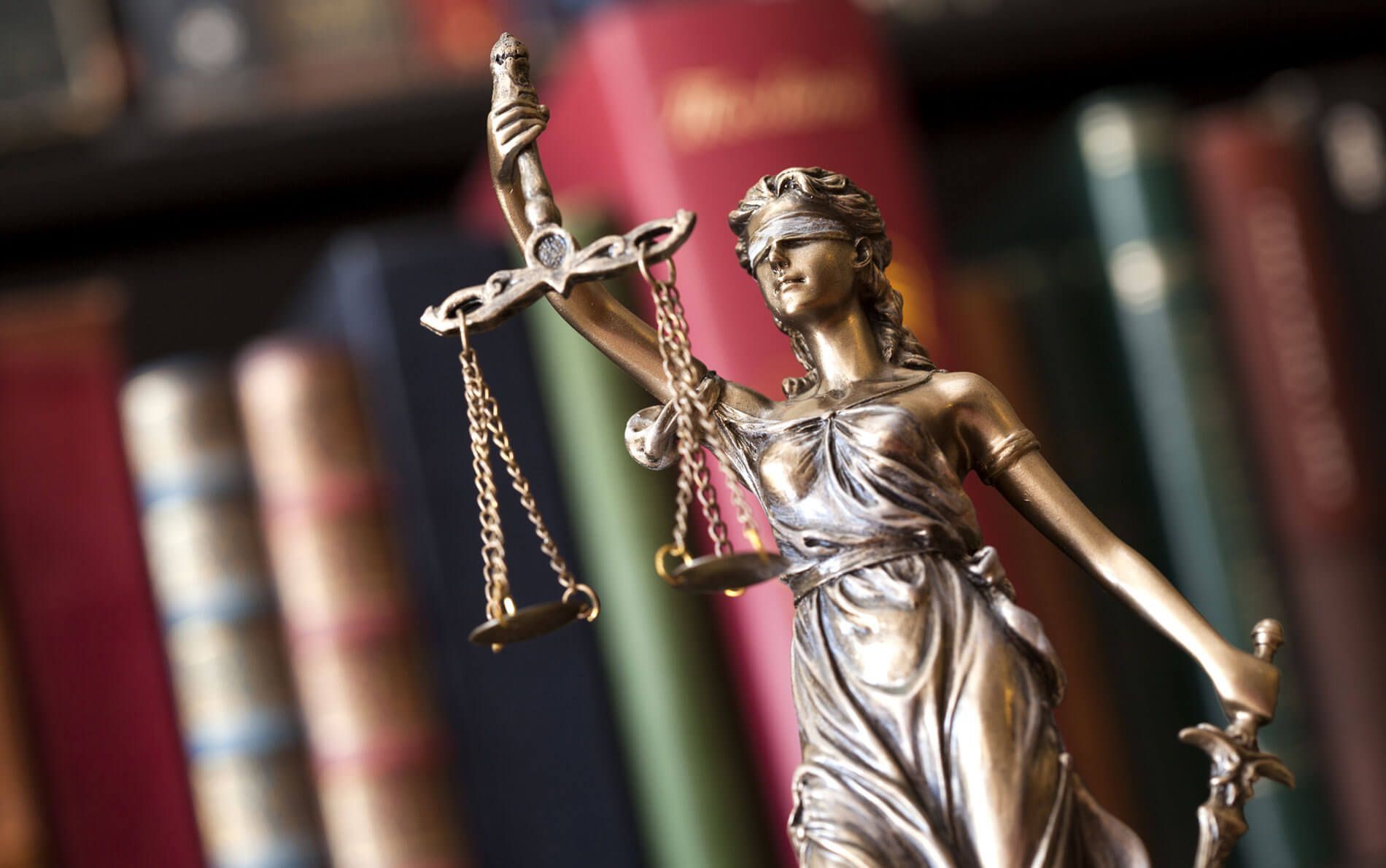 Una estatua de la Dama de la Justicia está parada frente a un estante de libros.