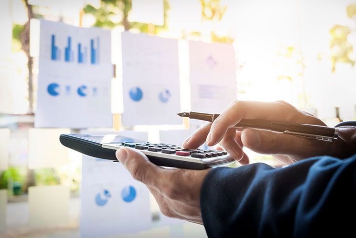 Persona que utiliza una calculadora con gráficos financieros en el fondo.