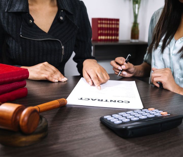 Dos personas revisando un contrato en un escritorio con un mazo y una calculadora.