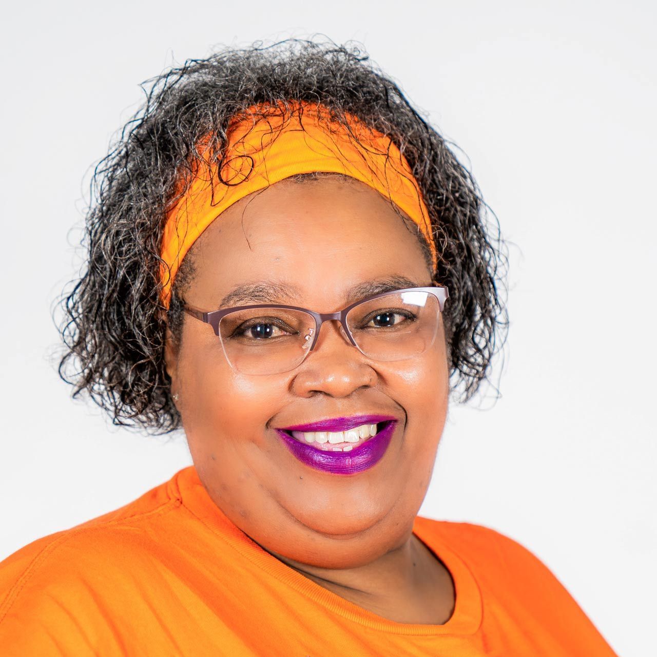 A woman wearing glasses and a headband is smiling for the camera in a southern caregivers t shirt