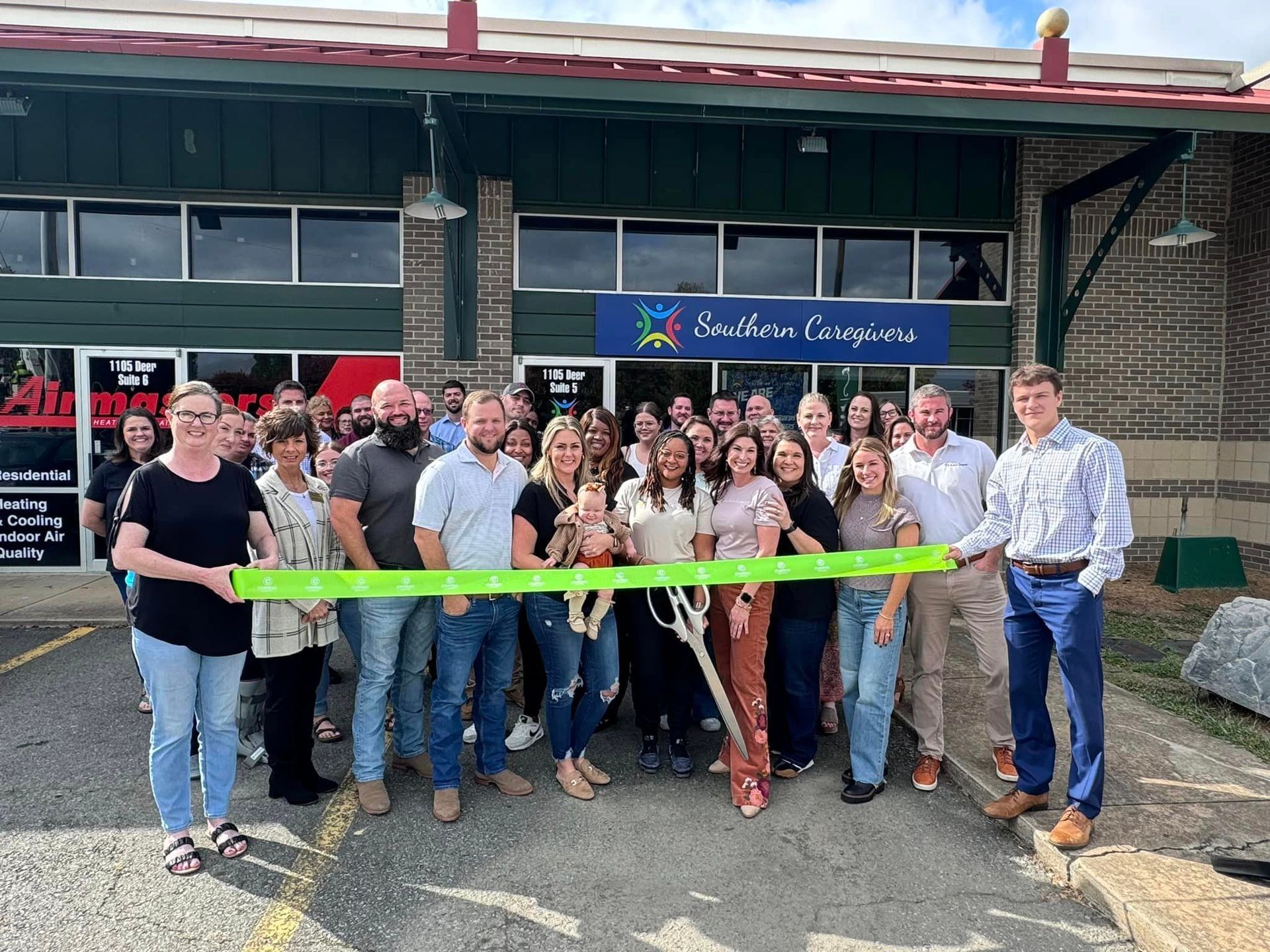 people standing in front of a southern caregivers building in Conway, AR holding a green ribbon for their grand opening.