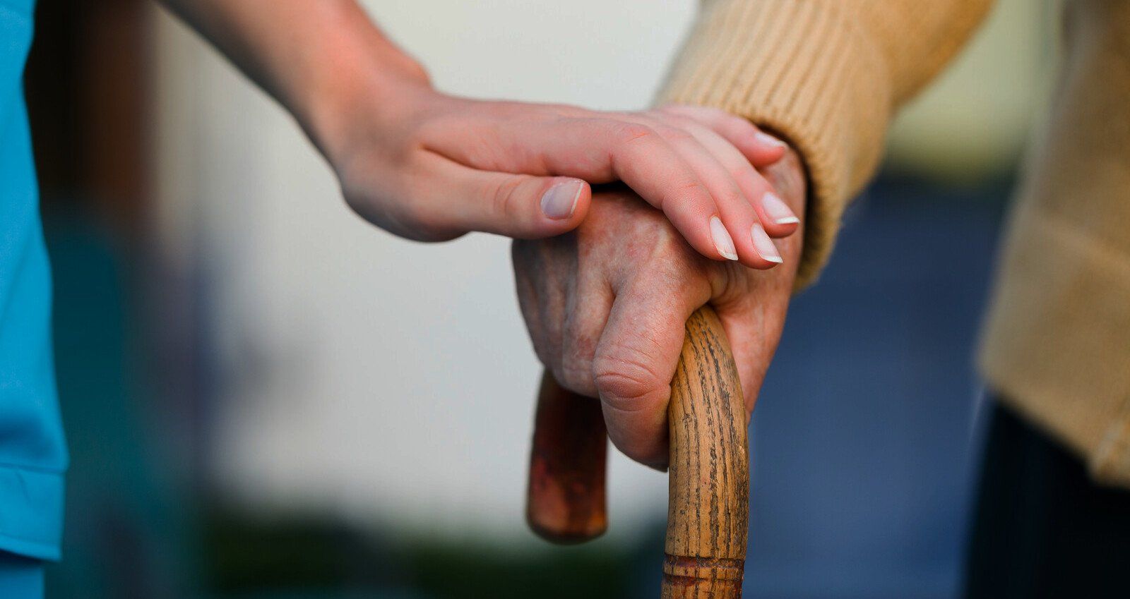 A nurse is holding the hand of an elderly woman holding a cane.