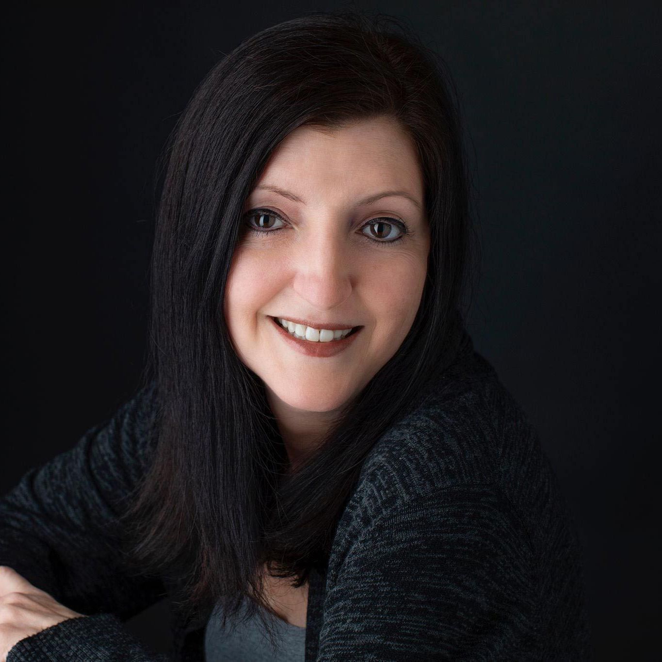 A woman with long dark hair is smiling in front of a black background. caregiver in northwest ar