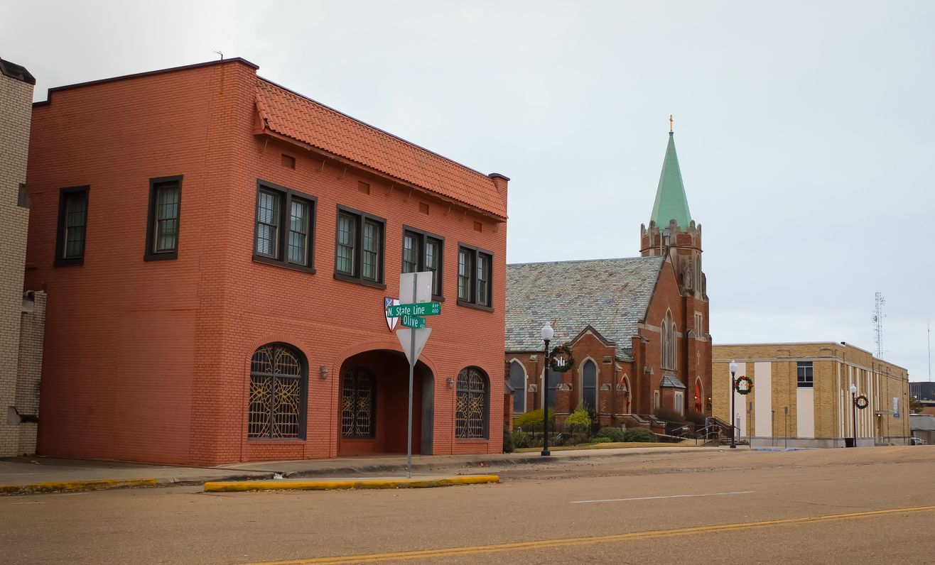 A brick building with a green steeple sits next to a church. Southern Caregivers building in Texarkana, AR.