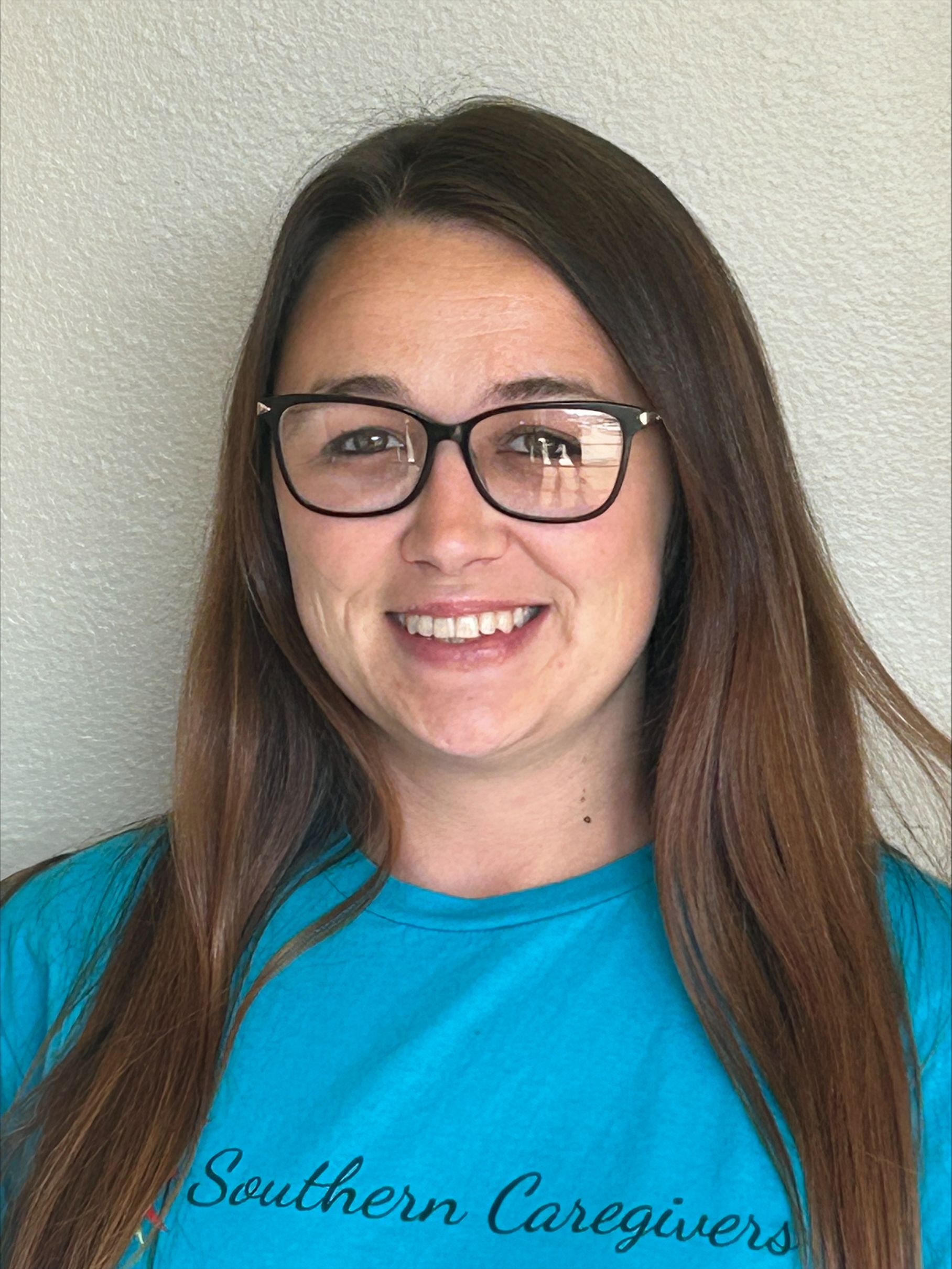 Woman with glasses, smiling, wearing a teal shirt with