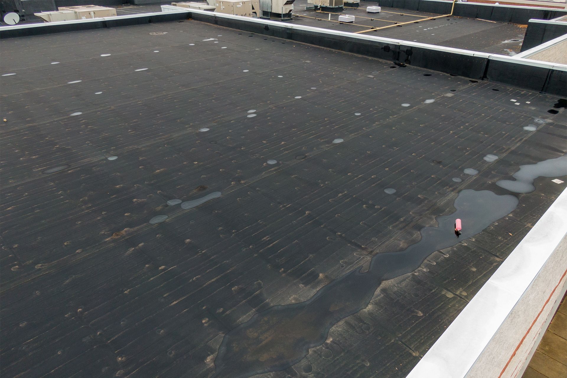 Flat, black commercial rooftop with standing water and a few visible objects, possibly HVAC units.