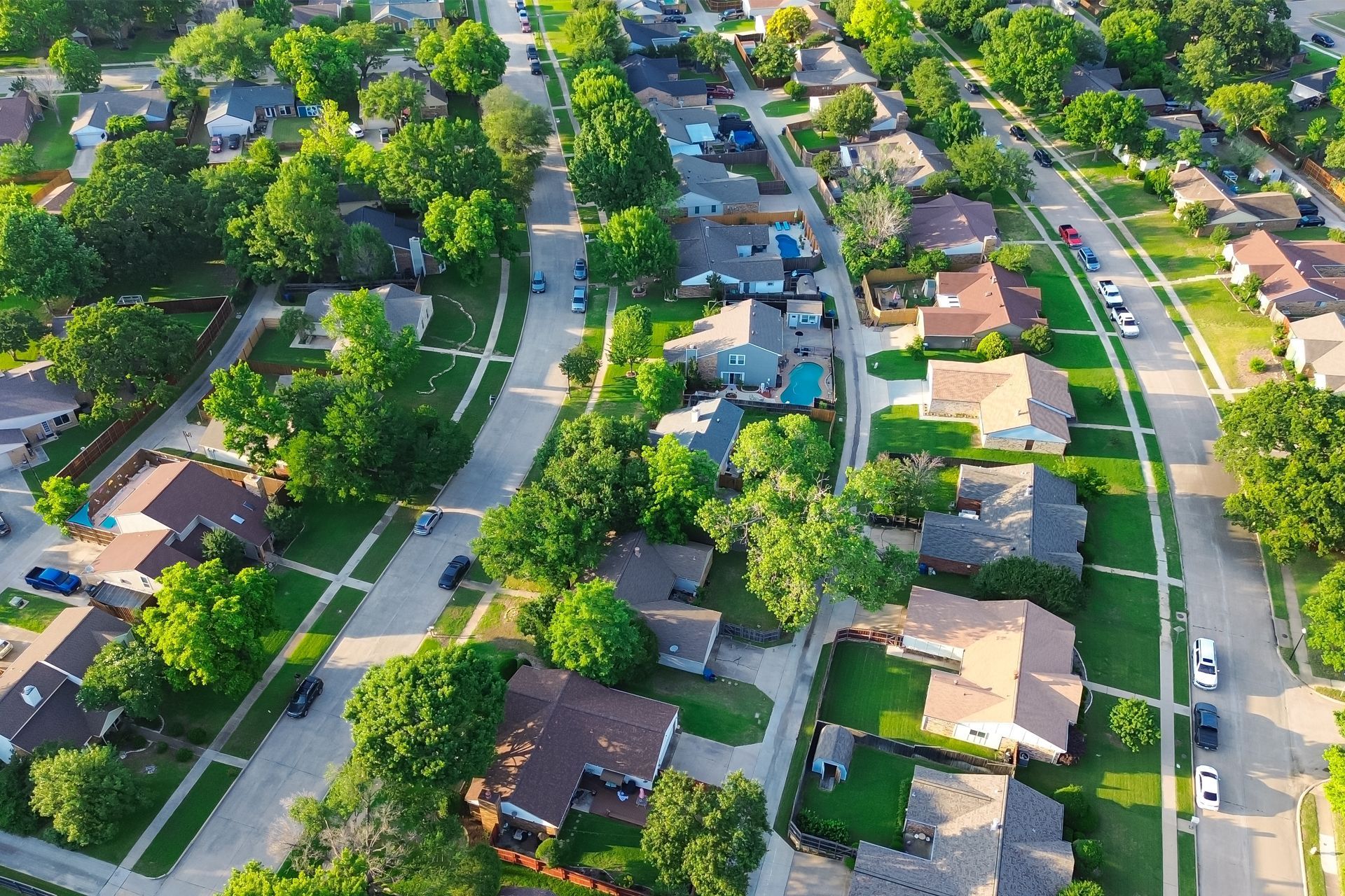 Aerial view of a suburban neighborhood with houses, green lawns, and tree-lined streets.