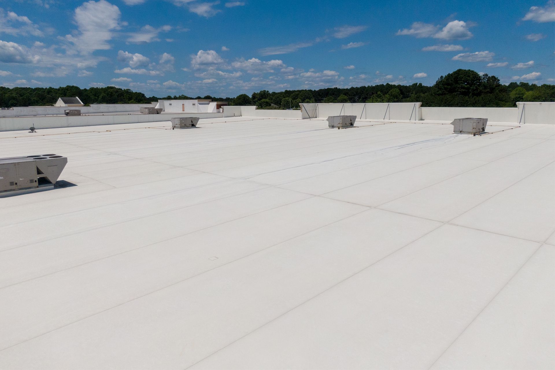 Bright white commercial flat roof with AC units, against a blue sky and tree line.