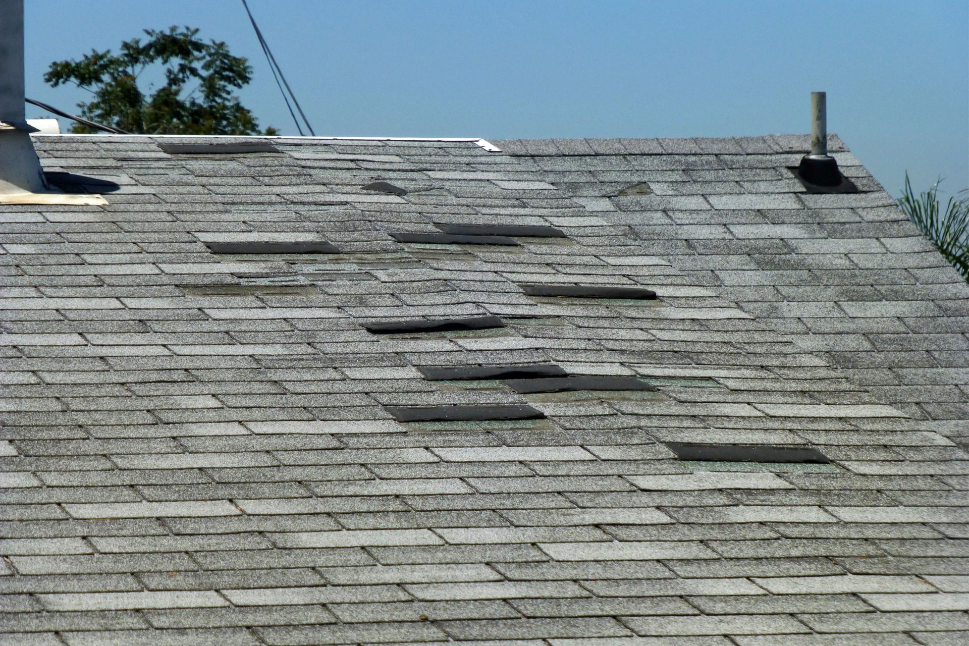 Damaged asphalt shingle roof with multiple missing shingles.