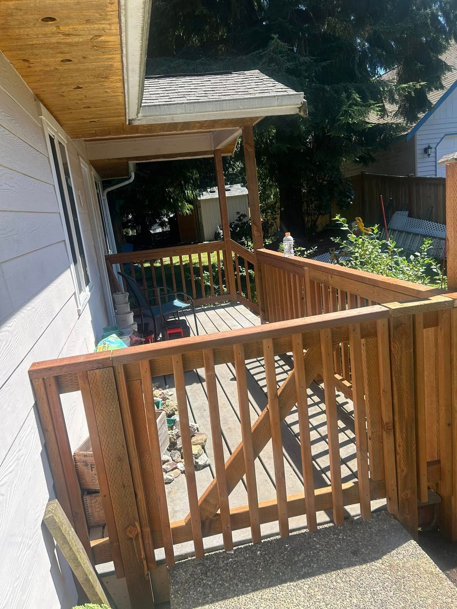 Wooden deck with railing, partial roof, and gate, next to a building; outdoor setting.