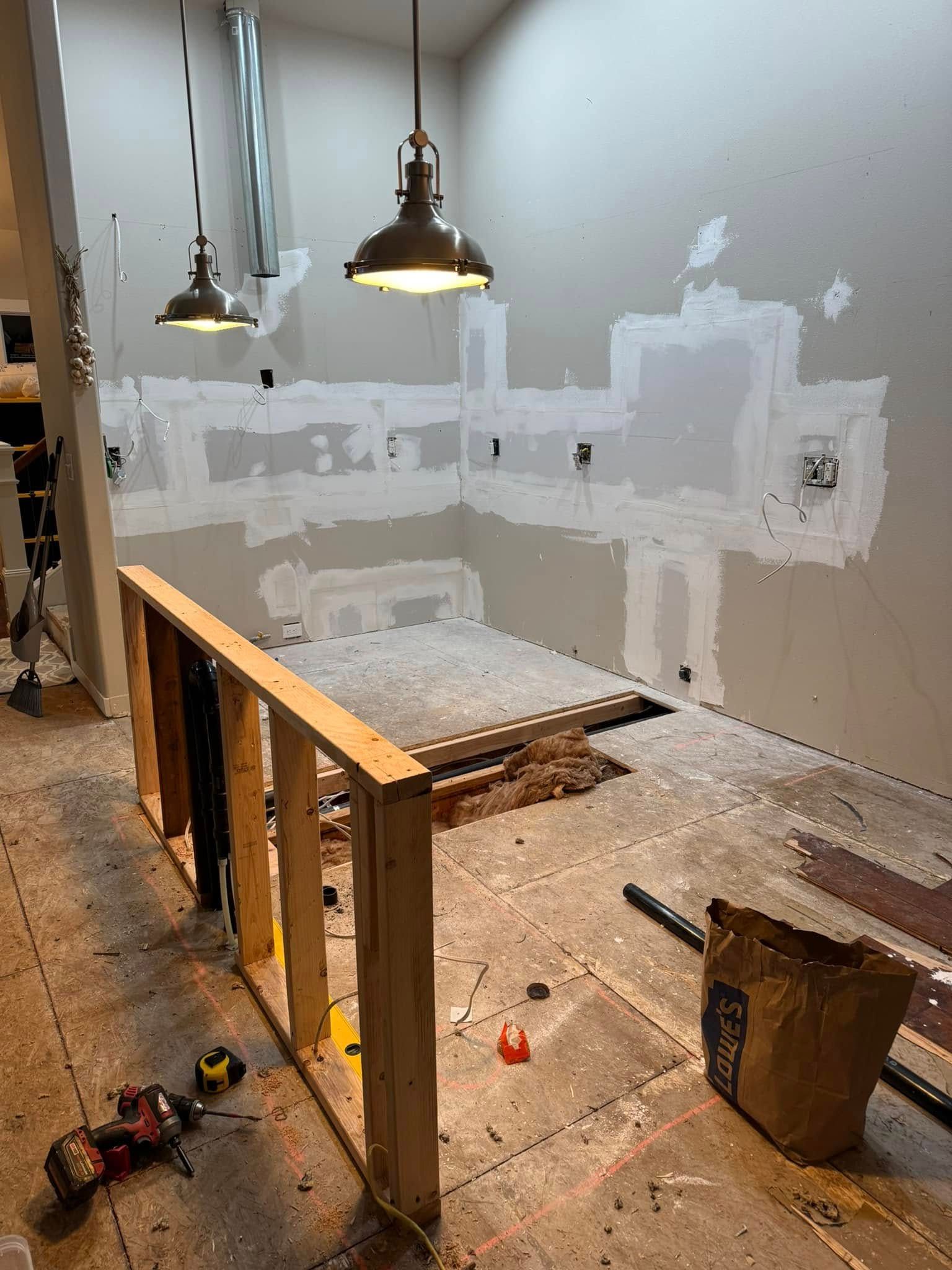 Interior renovation: unfinished wall with patched areas, new wood framing, two pendant lights, and construction debris.