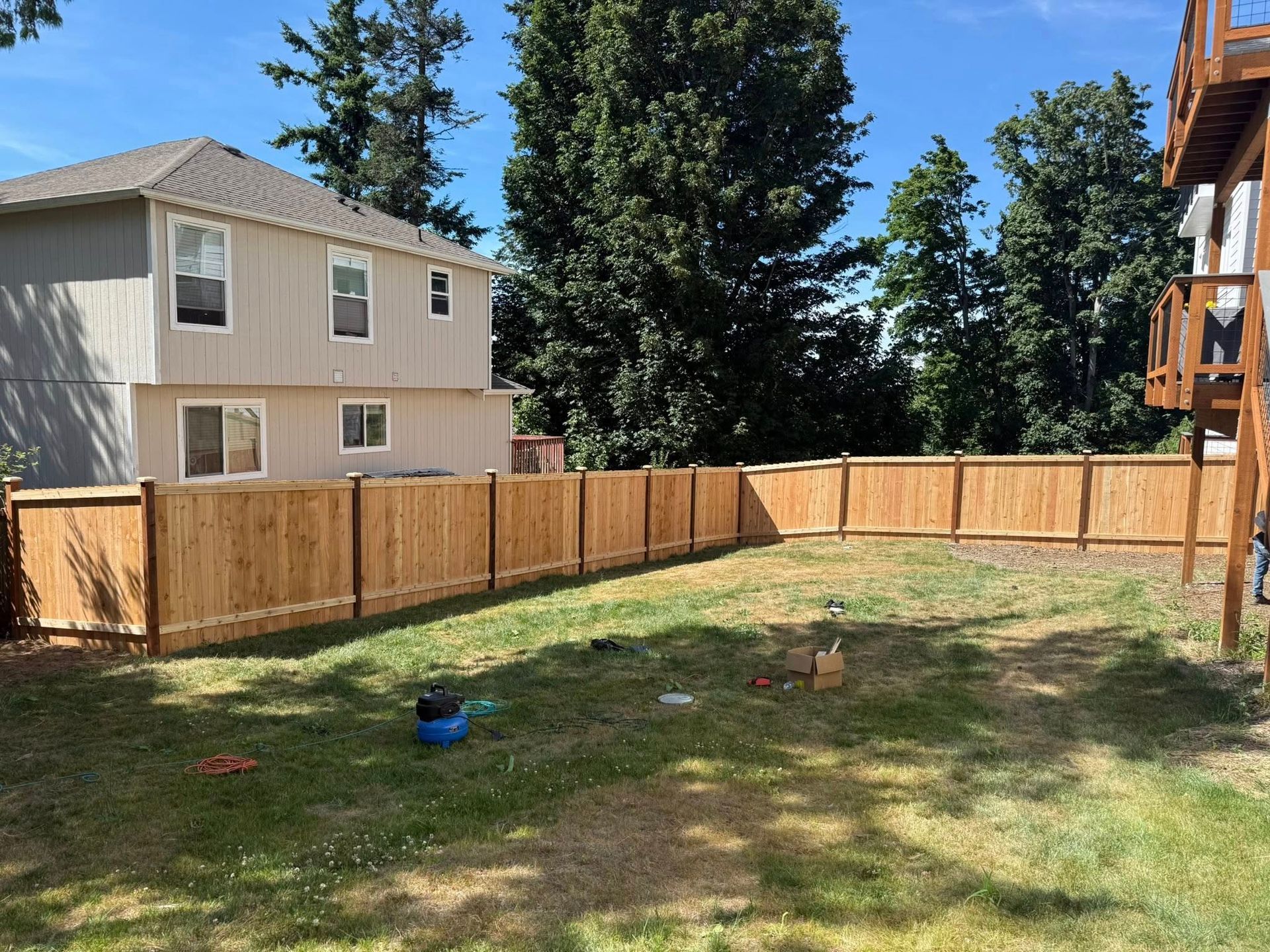 A newly fenced backyard with green grass and a two-story house in the background on a sunny day.