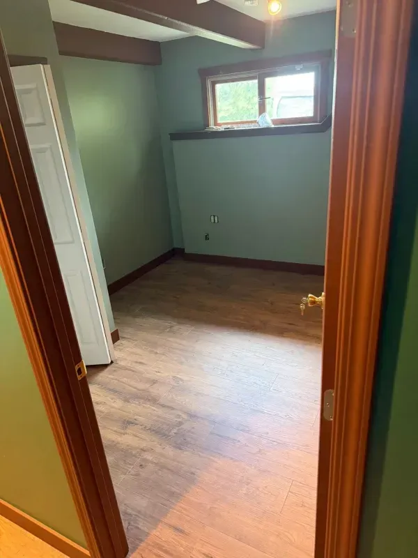 Empty room with green walls, brown trim and wood-look flooring, viewed from the doorway.