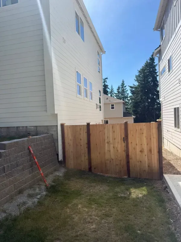 Wooden fence separating two beige houses, green lawn in between.