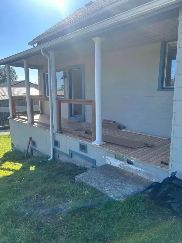 House with partially constructed wooden deck and siding, next to green lawn, under blue sky.