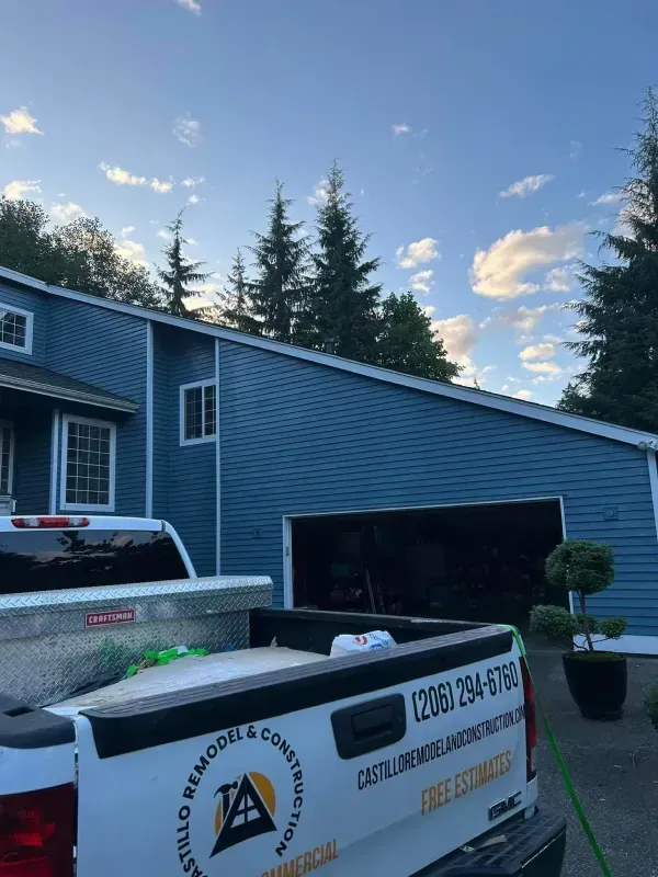 Blue house with an open garage and a work truck in front, under a cloudy sky.