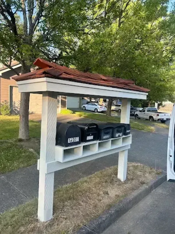 A row of black mailboxes under a white, covered structure with a red roof, beside a road.