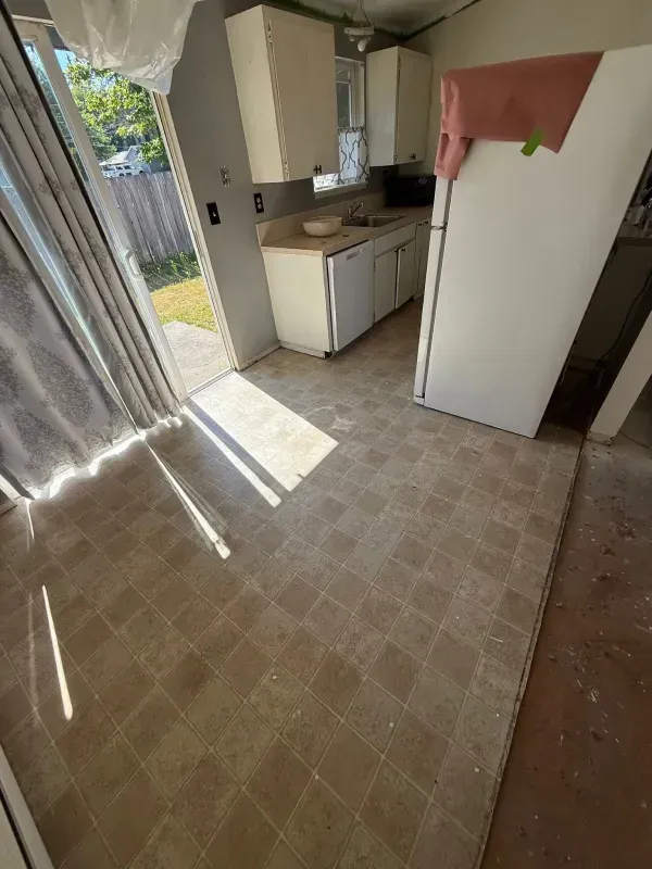 Kitchen with off-white cabinets and appliances, old tile floor, and a sliding glass door to a backyard.