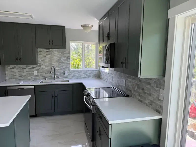 Dark gray kitchen cabinets with white countertops and tile backsplash.