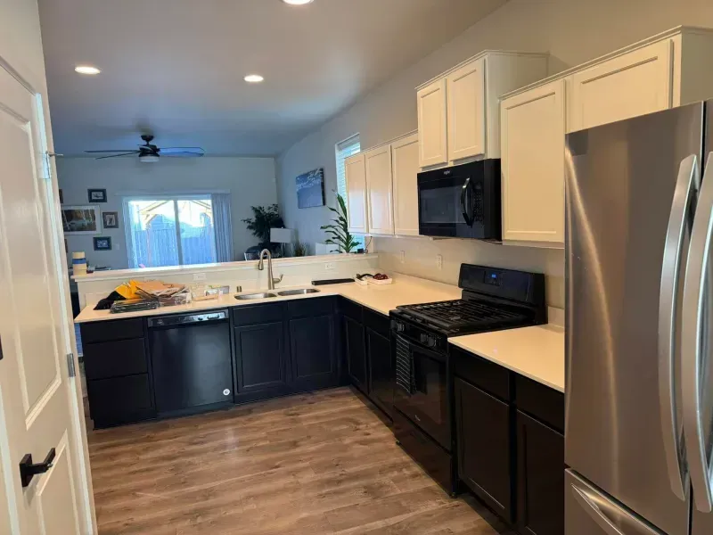 Kitchen with dark lower cabinets, white upper cabinets, stainless steel appliances, and wood-look flooring.