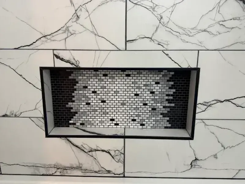 White marble tile shower wall with a recessed shelf of small brick-like tiles in black and white.