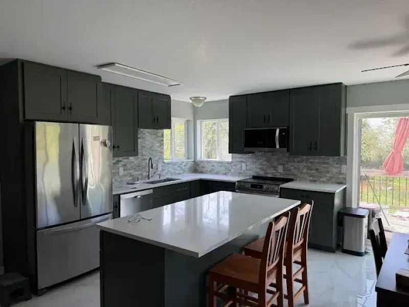 Modern kitchen with dark green cabinets, stainless steel appliances, and a white countertop island.