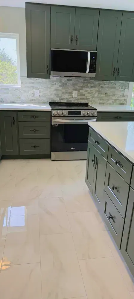 Green kitchen cabinets, stainless steel appliances, white countertops, and light-colored tiled floor.