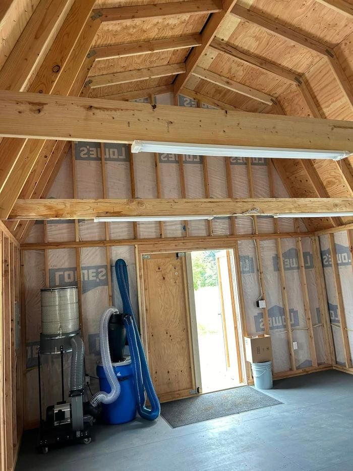 Interior view of a wooden workshop with insulation, an open door, and equipment.