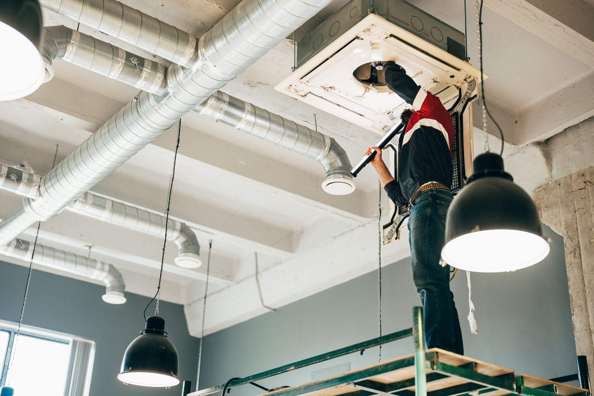 Technician performing maintenance on a ceiling-mounted air conditioning unit.