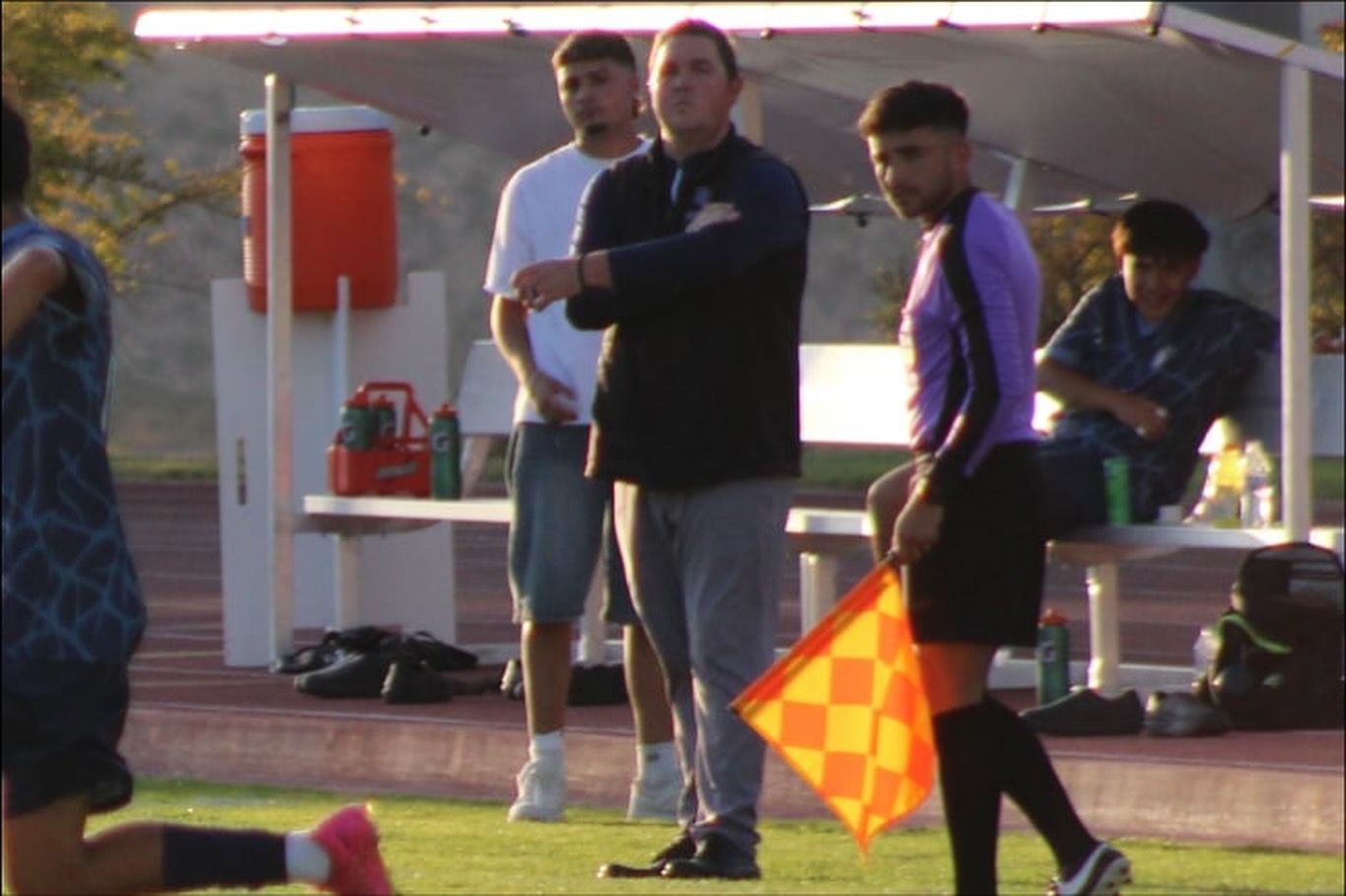 Joe Bouchelle watching on from the sideline in front of his team's bench during a match.