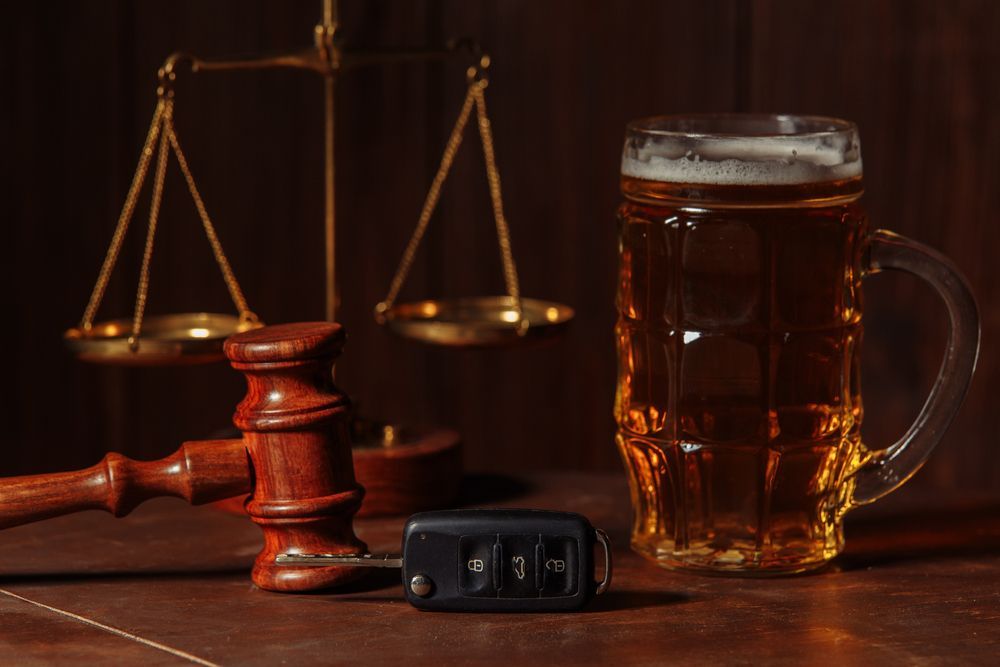 Scales of justice, gavel, car keys, and beer mug on a table, implying a legal or DUI-related theme.