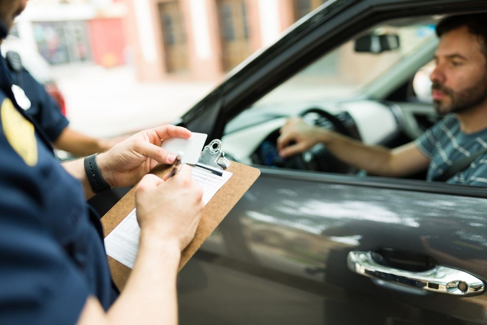 Police officer writing a ticket for a driver in a car.