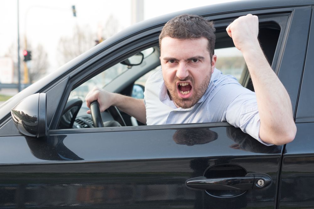 Man leaning out of a black car, yelling with a clenched fist.