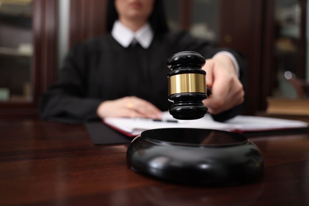 Judge holding a gavel above a wooden block, in a courtroom setting.