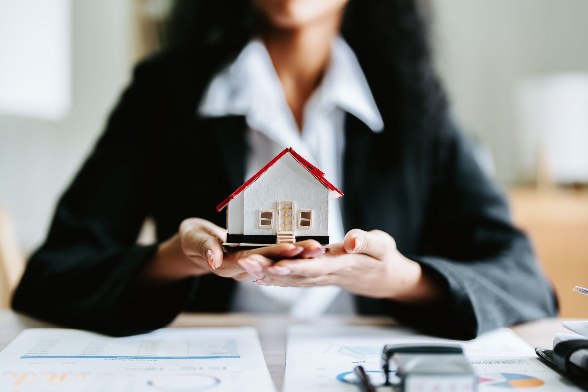 Person holding a small model house on a desk during a real estate meeting