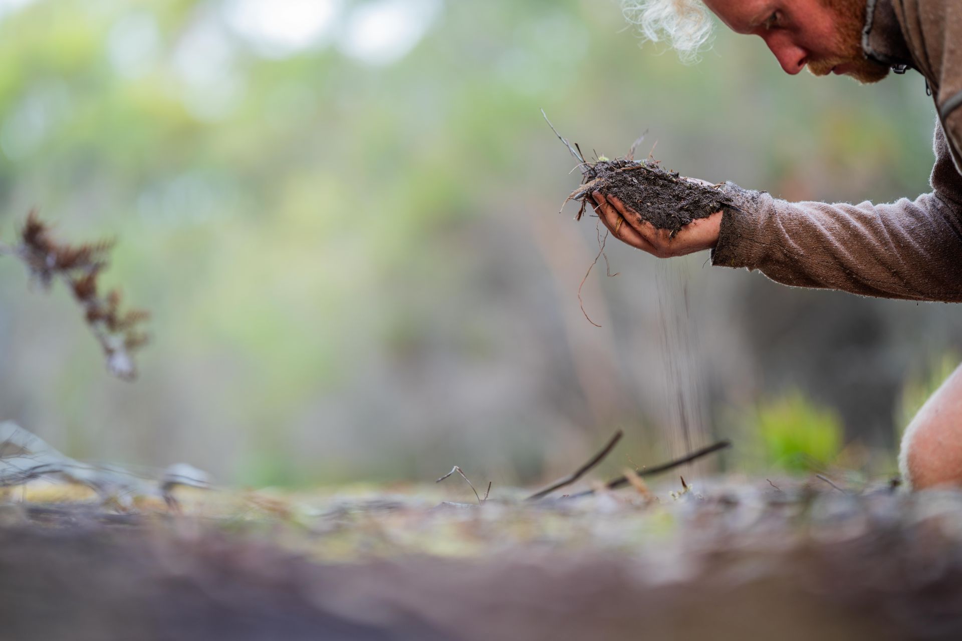 Person examining handful of dirt, possibly in a forest. Dirt is being thrown into the air. Person examining handful of dirt, possibly in a forest. Dirt is being thrown into the air.