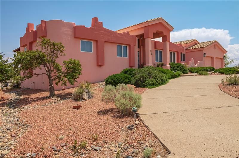 Pink stucco house with a concrete driveway against a desert landscape, blue sky.