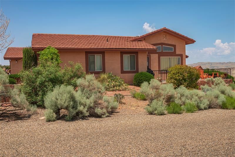Tan stucco house with red tile roof, surrounded by desert vegetation under a blue sky.