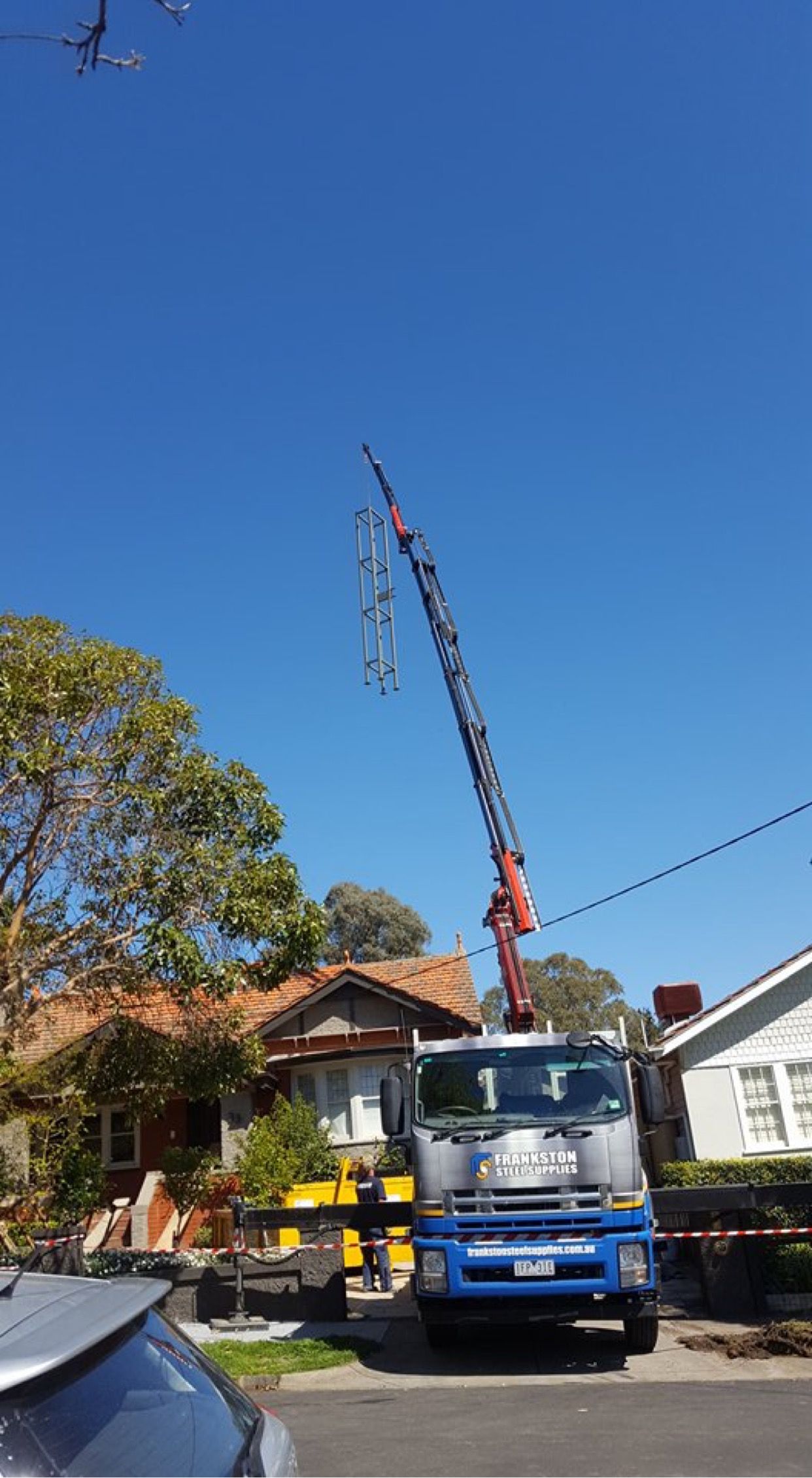 A blue truck with a crane on top of it is parked in front of a house.