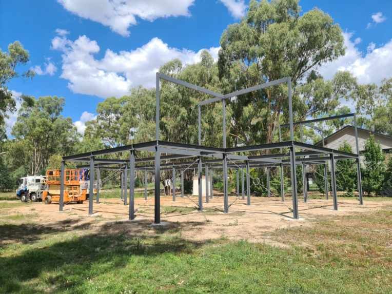 A large metal structure is being built in a field with trees in the background.