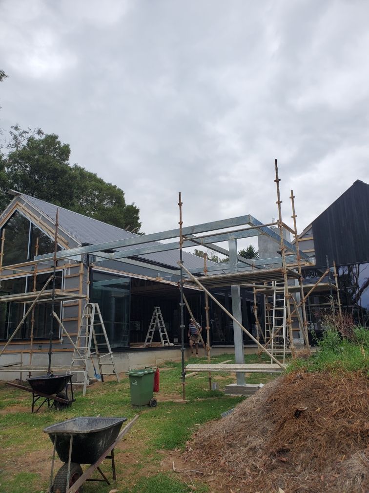 A house is being built with scaffolding and a wheelbarrow in front of it.